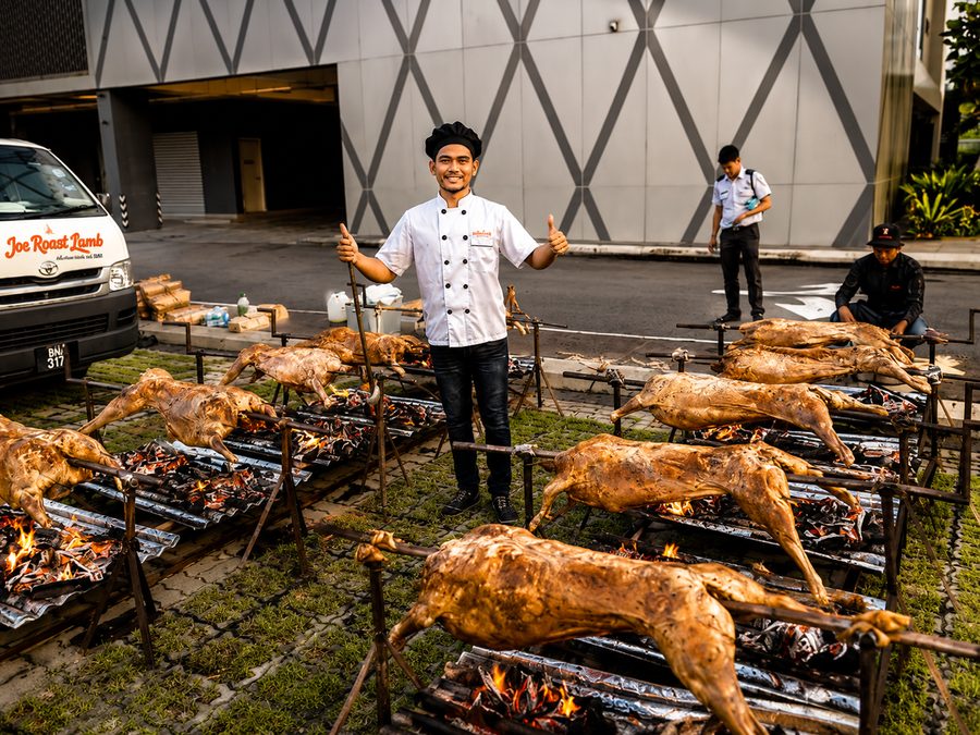A row of whole lambs roasting over open charcoal at a Joe Roast Lamb event